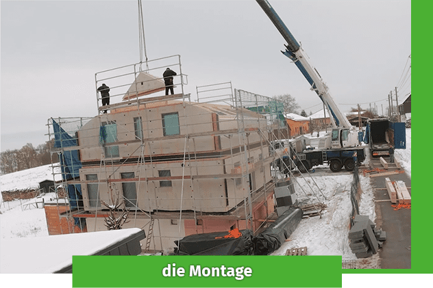 Enovia Haus Montage Baustelle mit Kränen und Arbeitern, die an einem Gebäude montieren. Winterliche Umgebung.