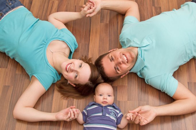 Ein Paar liegt auf dem Boden und hält ihren Baby-Sohn. Alle wirken glücklich.