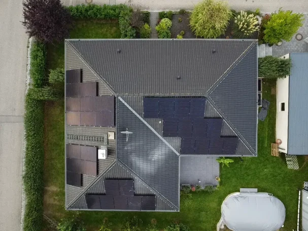 Dachansicht eines Hauses mit unterschiedlichen Dachpaneelen und umgebendem Garten.