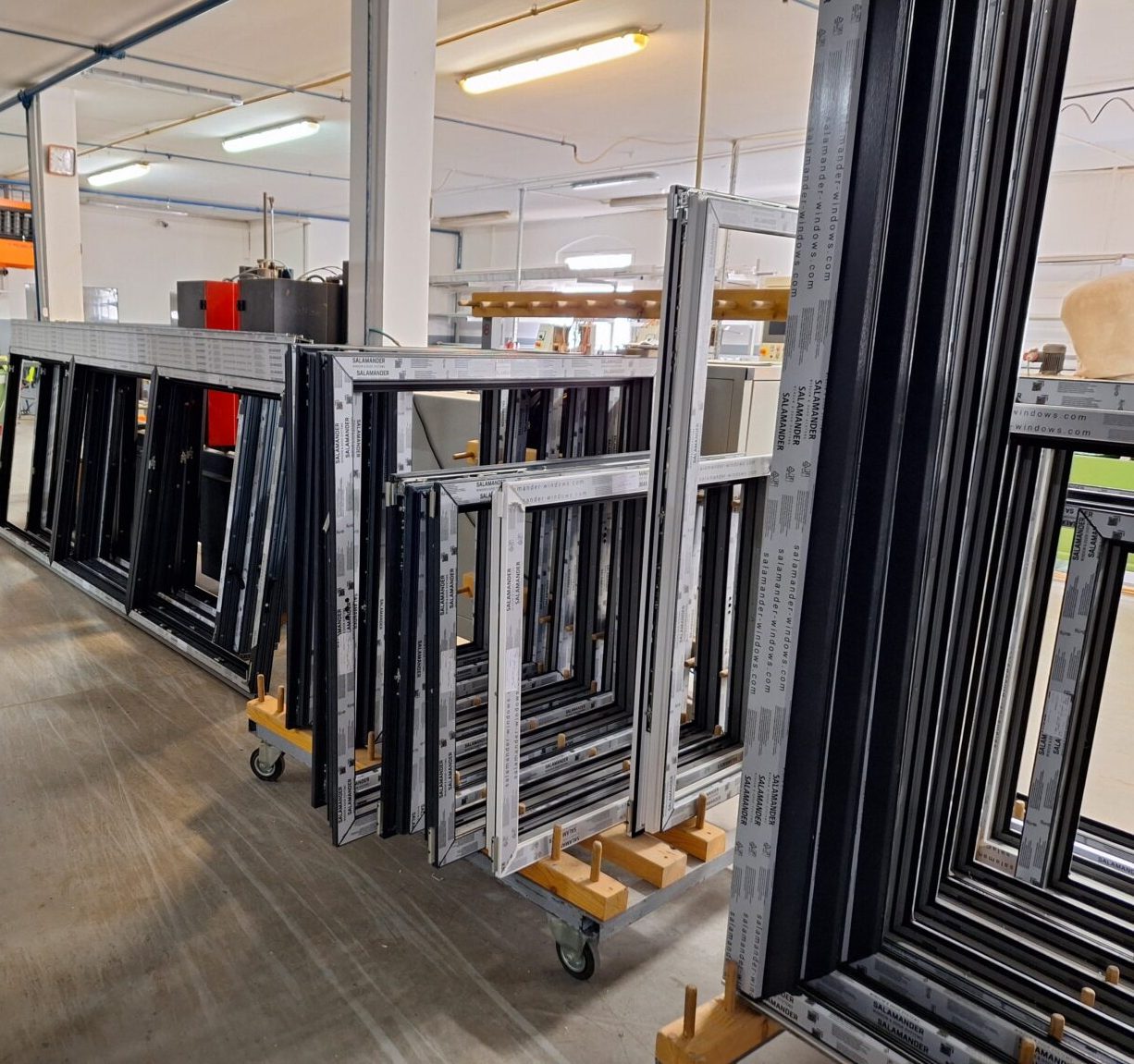 Enovia Haus Fenster Produktion Eine Reihe von Metallrahmen auf Rollwagen in einer hellen Werkstatt.