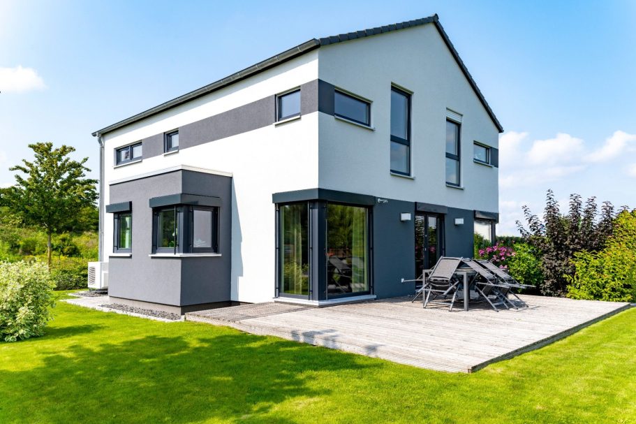 Modernes, zweigeschossiges Haus mit Garten und Holzterrasse unter blauem Himmel.
