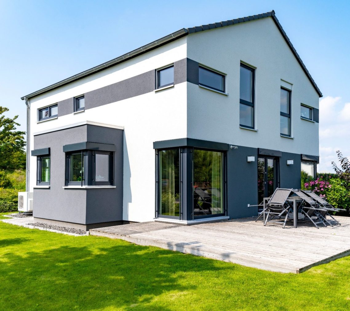 Modernes zweigeschossiges Haus mit großen Fenstern und grünem Garten.