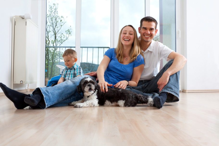 Familie sitzt auf dem Boden eines leeren Raumes mit einem Hund und einem Kind.