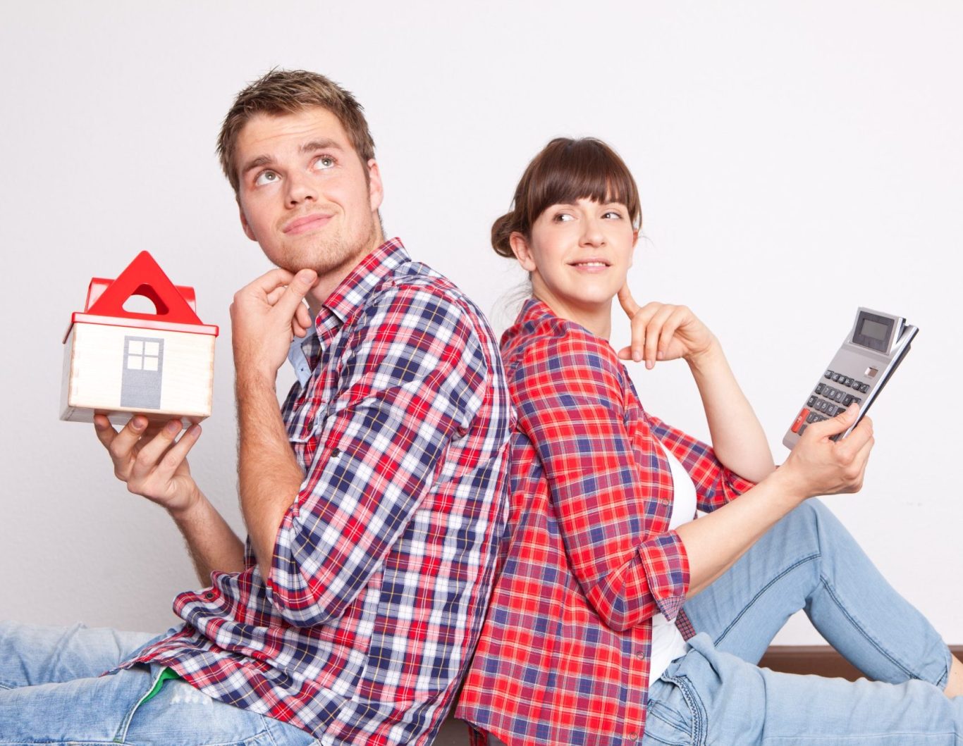 Junge hält ein Hausmodell, Mädchen liest ein Buch, beide sitzen Rücken an Rücken.