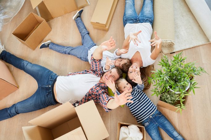 Familie liegt entspannt im Raum, umgeben von Umzugskartons und einer Pflanze.