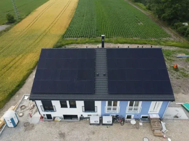 Ein Gebäude mit schwarzem Dach und Solarpanels, umgeben von Feldern.
