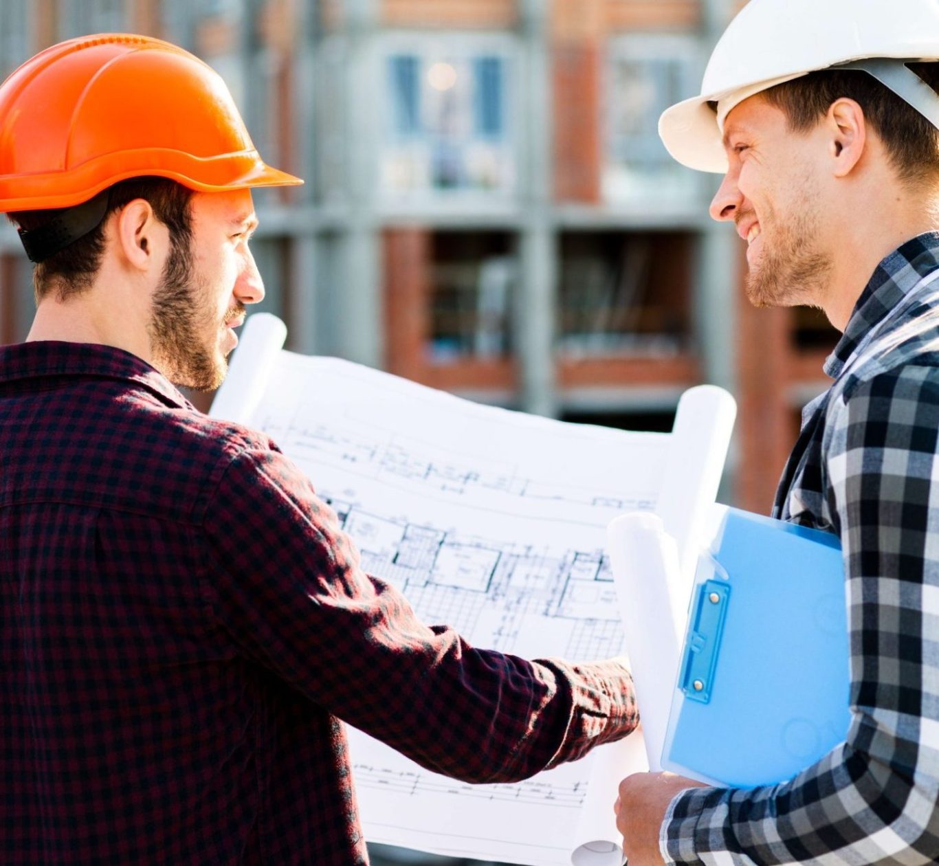 Zwei Bauarbeiter mit Helm betrachten Baupläne auf einer Baustelle.
