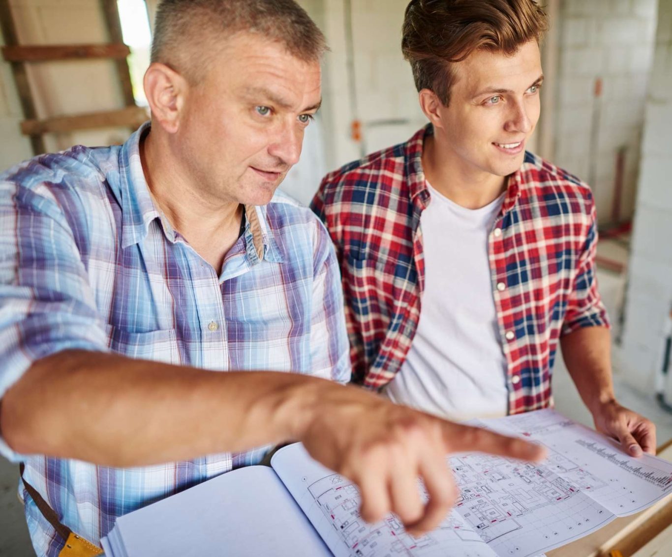 Zwei Männer betrachten Baupläne und diskutieren in einer Baustelle.
