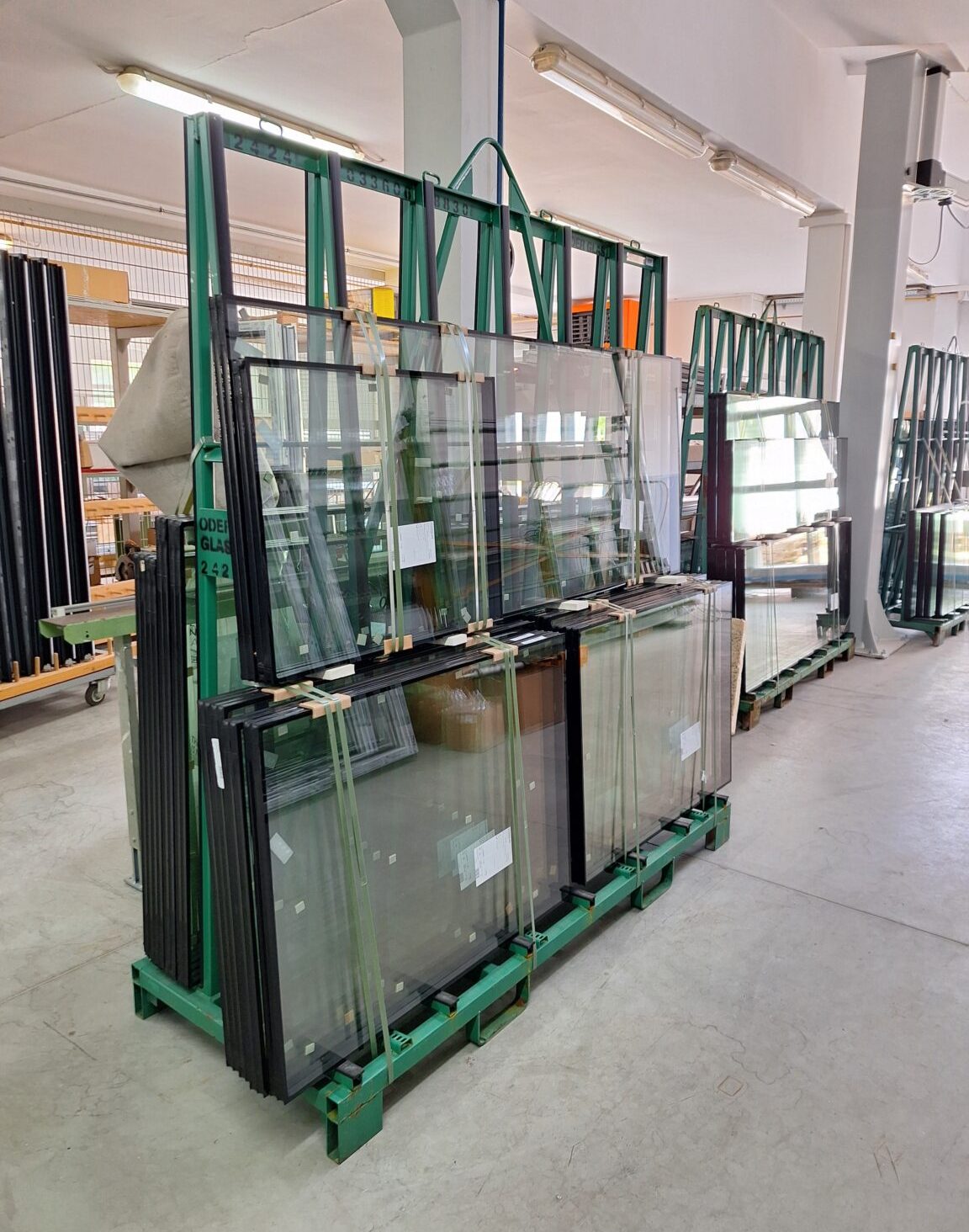 Enovia Haus Fenster Produktion Mehrere Glasscheiben stehen gestapelt auf einem Gestell in einer Lagerhalle.