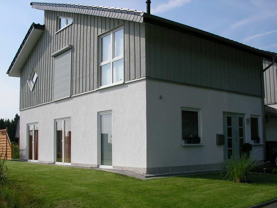 Modernes zweigeschossiges Haus mit grauer Fassade und großen Fenstern in einem Garten.