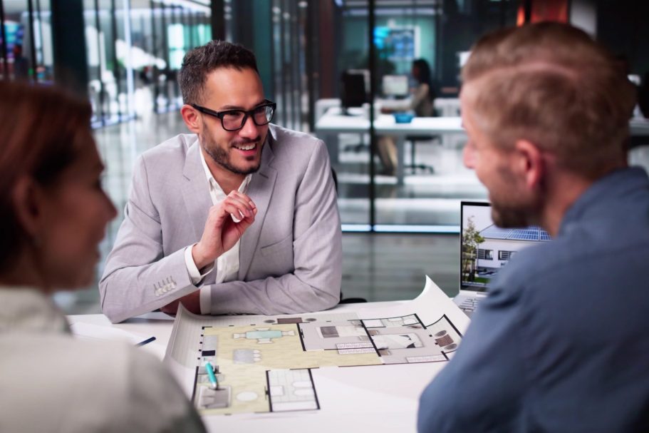 Drei Personen am Tisch diskutieren über Pläne und Entwürfe in einem modernen Büro.