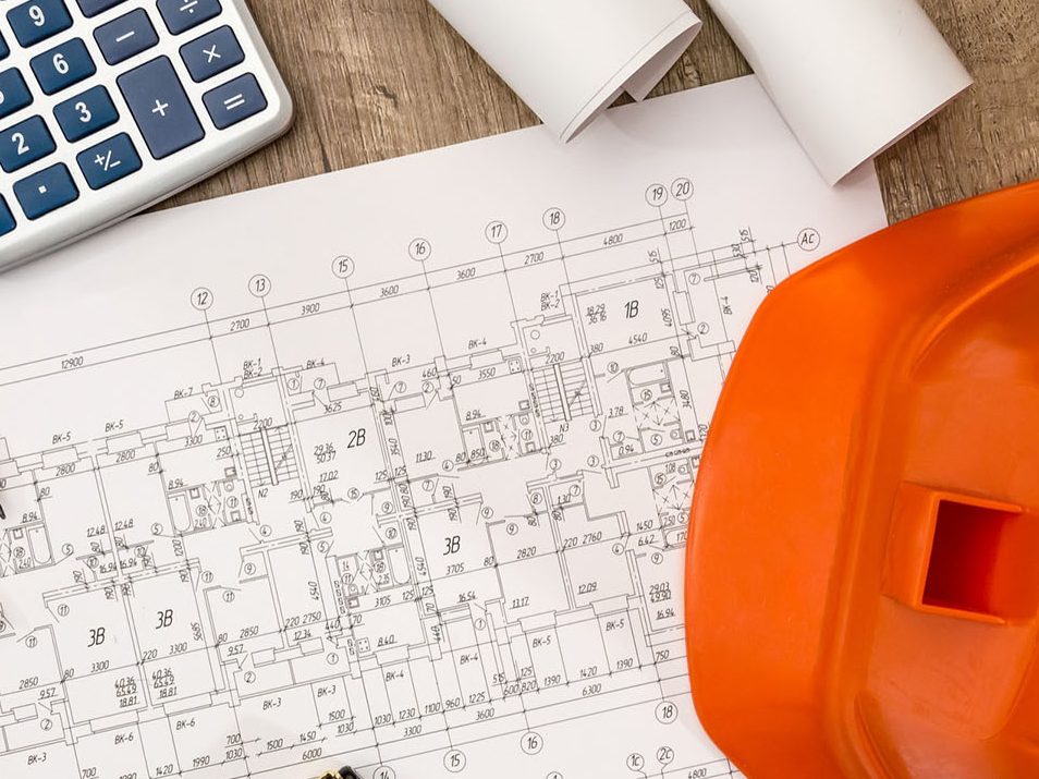 Baupläne, orange Sicherheitshelm, Taschenrechner und Schreibutensilien auf einem Tisch.