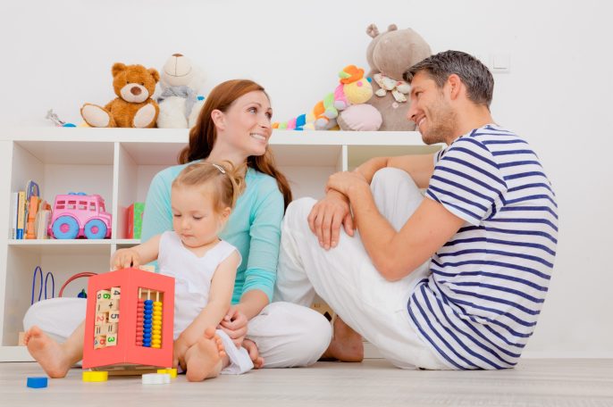 Familie spielt gemeinsam auf dem Boden in einem Kinderzimmer mit Spielzeug.