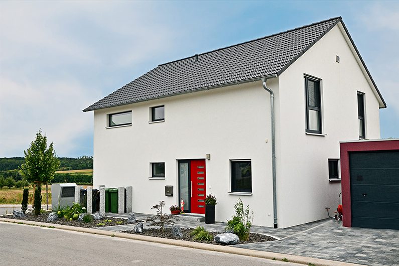 Modernes, zweistöckiges Einfamilienhaus mit roter Tür und umliegendem Garten.