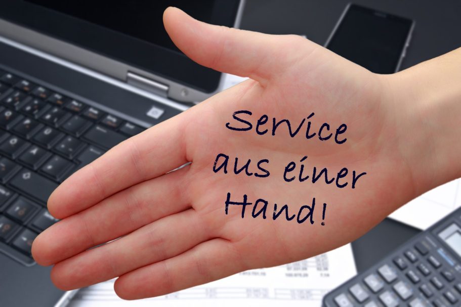 Hand mit der Aufschrift "Service aus einer Hand" vor einem Laptop und Tastatur.
