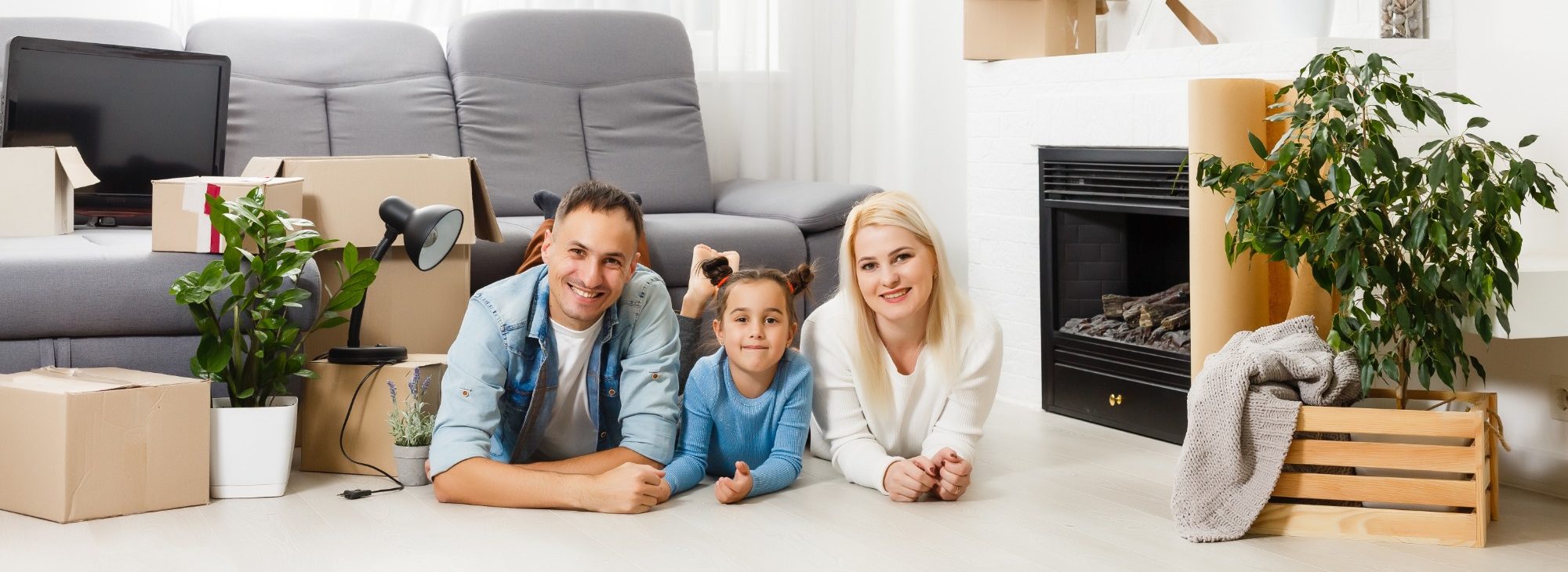 Familie liegt auf dem Boden eines Wohnzimmers mit Umzugskartons und Pflanzen.