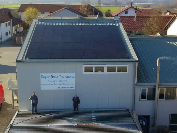 Zwei Personen stehen vor einem modernen Gebäude mit Solarpanelen auf dem Dach.